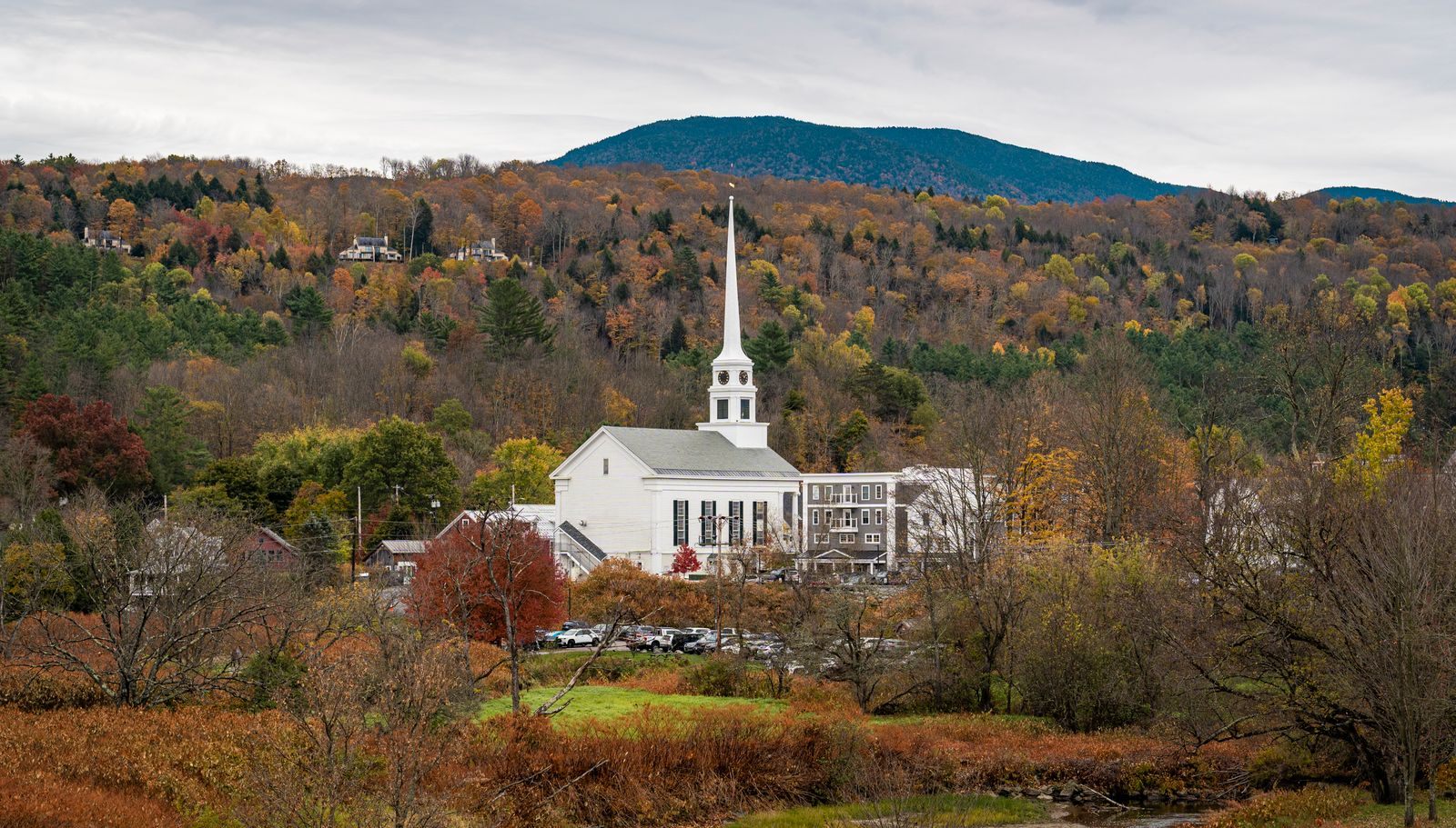 White church steeple among autumn trees below green mountains, a classic scene in one of the best small towns in America